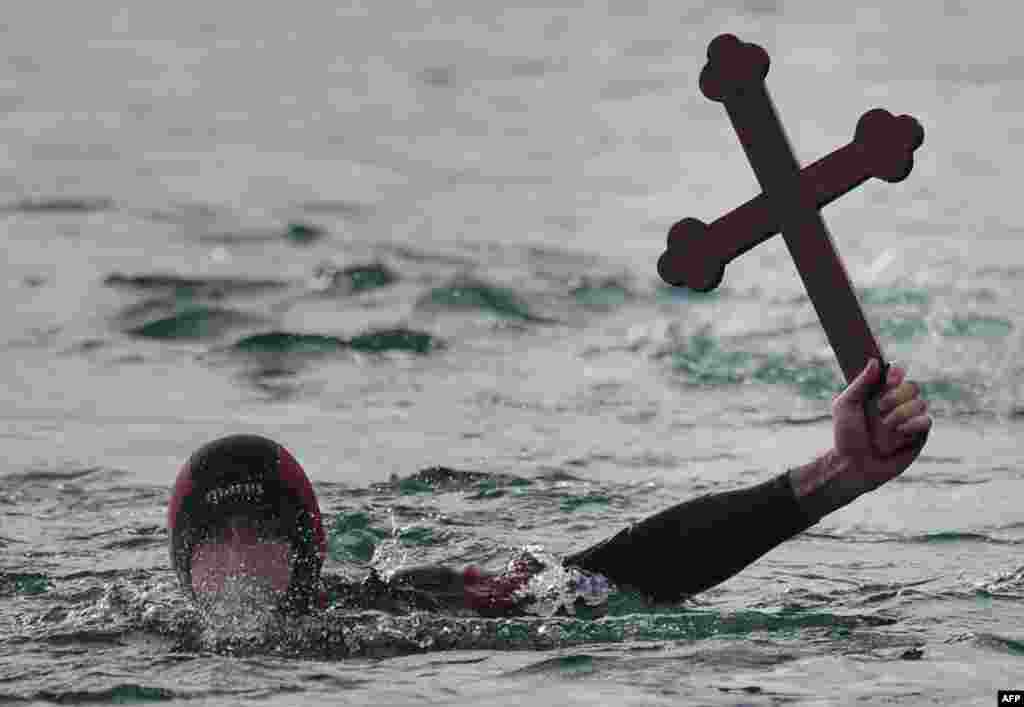 A Romanian diver shows a wooden cross he retrieved from the Black Sea during an Epiphany religious service in Constanta. Thousands of Romanian Orthodox believers attended the celebration in the Black Sea coastal city. (AFP/Daniel Mihailescu)