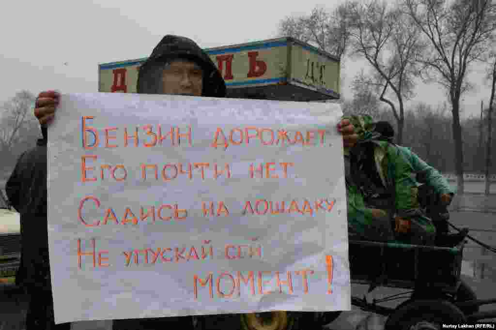Участник флеш-моба держит плакат с надписью: &laquo;Бензин дорожает, его почти нет, садись на лошадку, не упускай сей момент!&raquo;. 