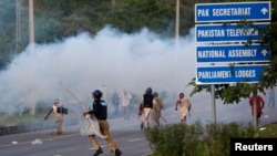 A policeman runs to disperse anti-government protester during the Revolution March towards the prime minister's house in Islamabad, September 1, 2014.