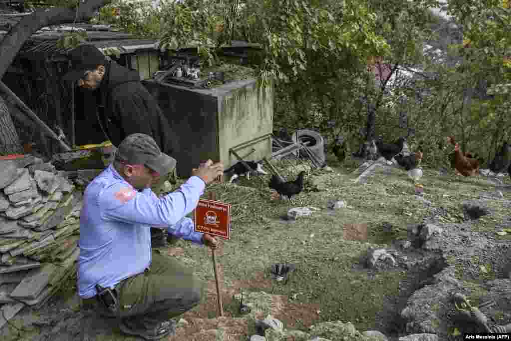 A member of the Halo Trust, a mine-clearing NGO, installs a sign warning of an unexploded rocket in a yard in Stepanakert on October 14.