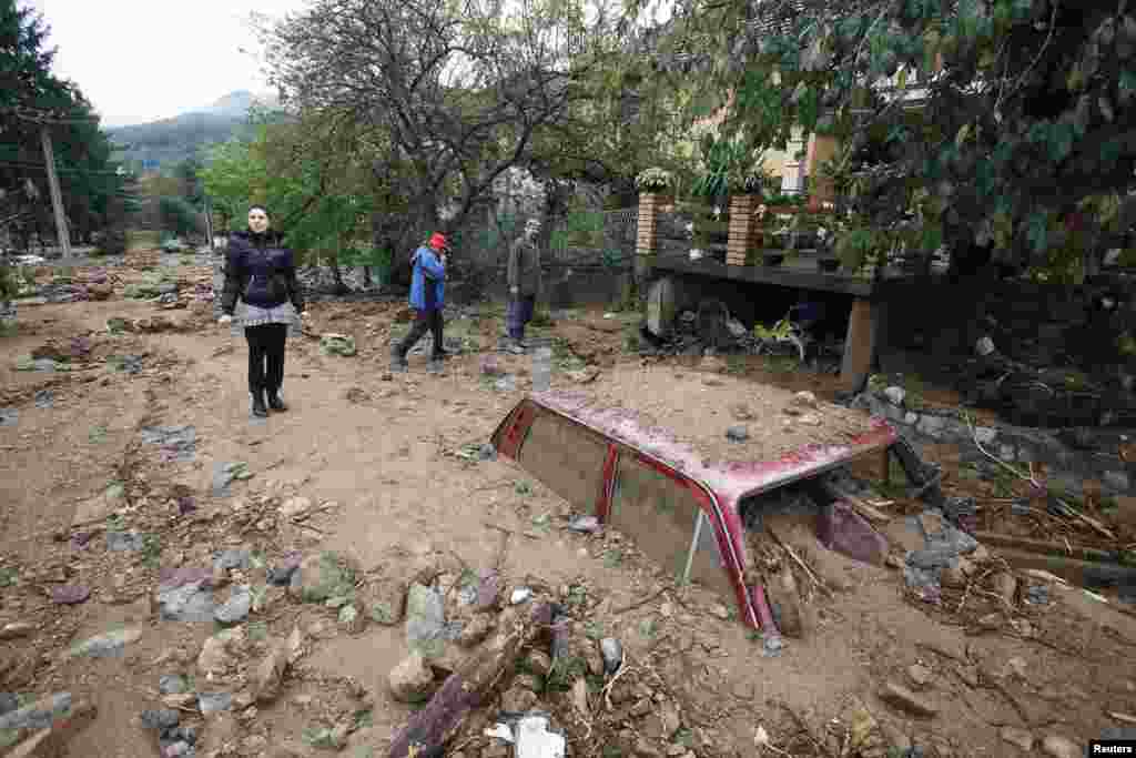 People walk past a vehicle almost entirely submerged in mud after heavy flooding in the village of Tekija, Serbia, on September 17. (Djordje Kojadinovic, Reuters)