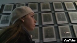 Yevgenia Karatygina in front of portraits of Holocaust victims in a still from the trailer for the documentary "Holocaust -- Wallpaper Paste?"