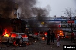 Ljudi pored objekata i vozila zapaljenih u ruskom napadu raketama i dronovima na Kijev, 29. novembra 2025.