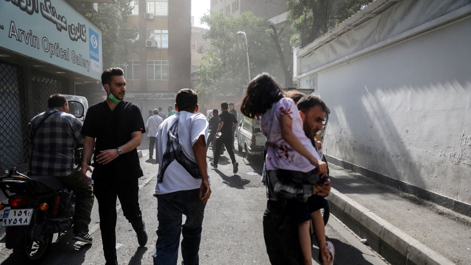 Iran -- People run along a street amid smoke following the Israeli strikes on Iran