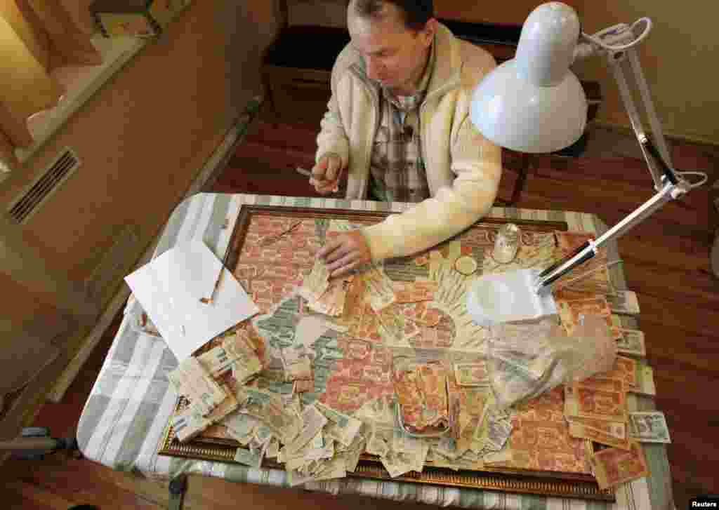 Менскі мастак Ігар Арыніч робіць каляж з савецкіх грошай. (Фота Васіля Федасенкі, Reuters)
