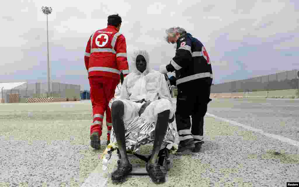 Red Cross members help a migrant after he disembarked in the Sicilian harbor of Augusta. The bodies of 17 migrants were brought ashore in Sicily aboard an Italian naval vessel along with 454 survivors as efforts intensified to rescue people fleeing war and poverty in Africa and the Middle East. (Reuters/Antonio Parrinello)