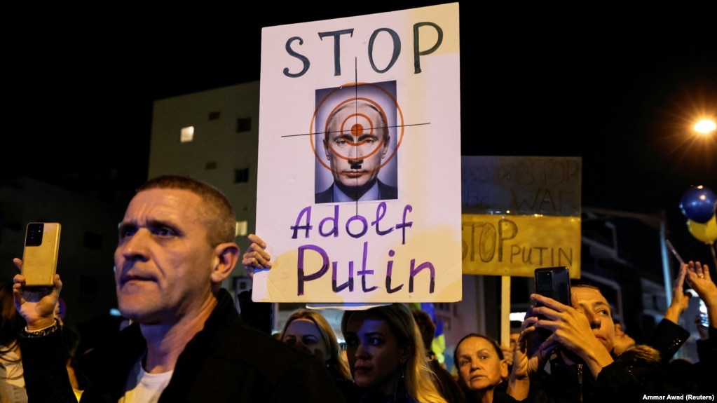 معترضان به حمله نظامی ولادیمیر پوتین به خاک اوکراین با در دست داشتن پلاکاردی، او را با هیتلر مقایسه می‌کنند- تجمع مقابل سفارت روسیه در تل‌آویو