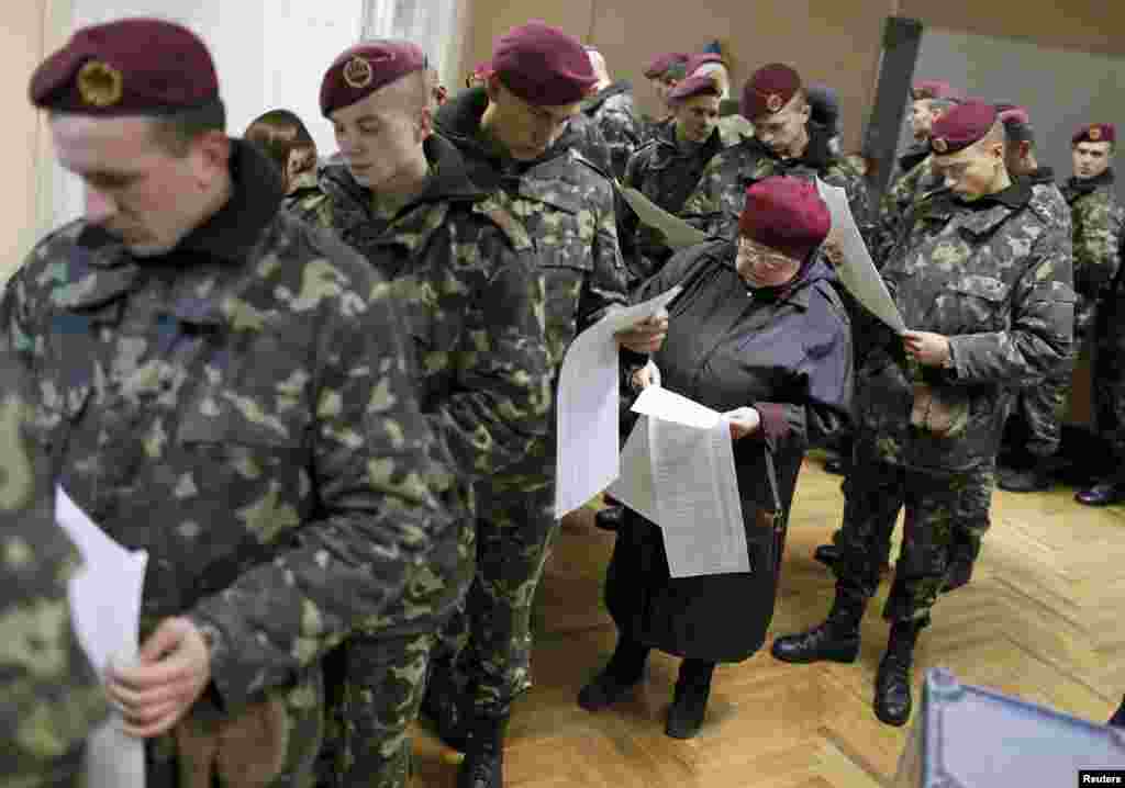 Украинские военнослужащие и пожилая женщина стоят в очереди с бюллетенями в день голосования на выборах в Верховную Раду. Киев, 26 октября 2014 года. 