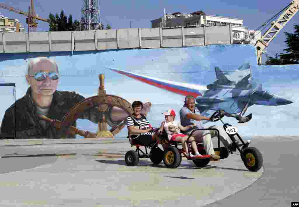 A family rides a quadracycle past a mural depicting Russian President Vladimir Putin in the Crimean city of Yalta. Crimea was illegally annexed from Ukraine by Russia last year. (AFP/Max Vetrov) 