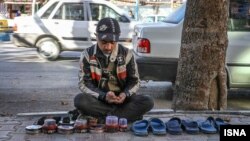 An Iranian boy who ploishes shoes waits for a customer in a street, Feb 2015