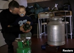 Capelanul militar Anton Ribikov își îmbrățișează fiul de doi ani, Matvii, în timp ce încălzește apă la butelie în timpul unei pene de curent.