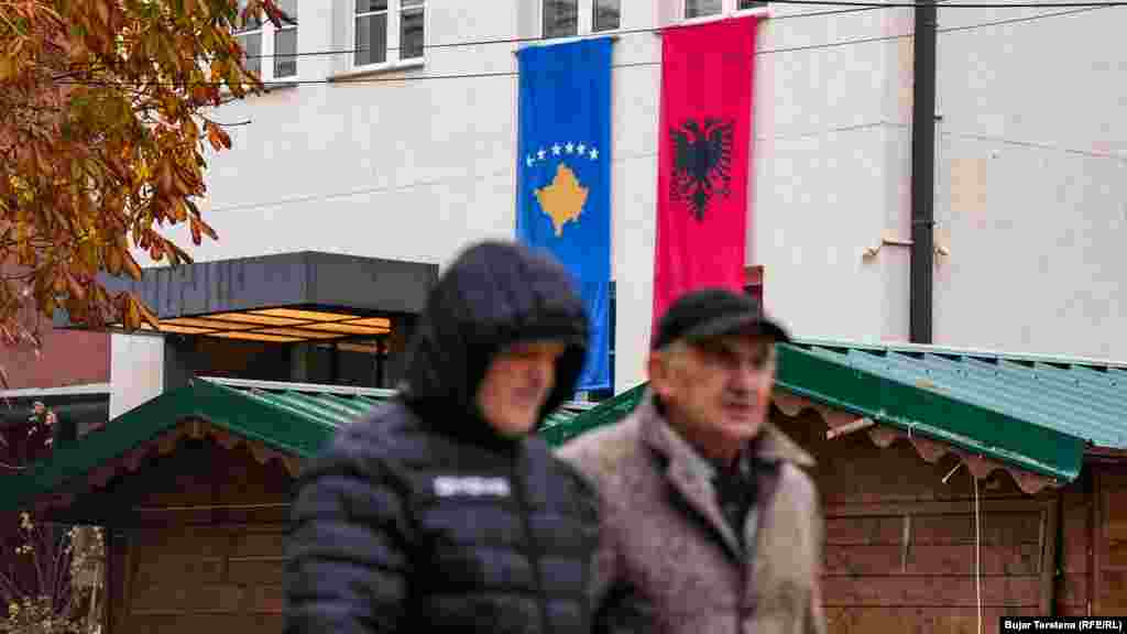 Dy burra kalojnë në sheshin e Prishtinës, ku në një ndërtesë janë vendosur flamuri i Kosovës dhe ai i Shqipërisë. 