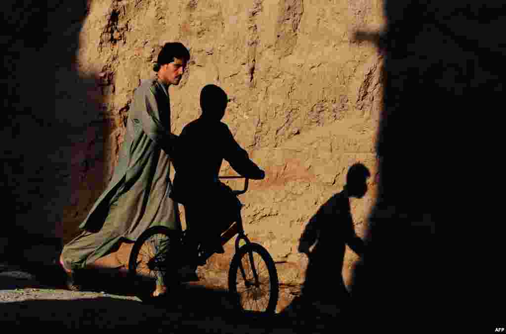 An Afghan child is silhouetted as he rides past a pedestrian in a street on the outskirts of Herat. (AFP/Aref Karimi)