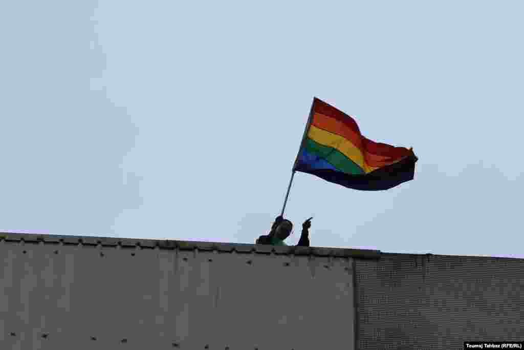 یکی از شهروندان بر بام خانه&zwnj;اش پرچم رنگین&zwnj;کمان را در دست گرفته&zwnj;است؛ پرچمی که قدمتی نسبتا طولانی دارد، و هرچند این روزها بیشتر به&zwnj;یادآورنده جنبش برابری&zwnj;خواهانه دگرباشان و همجنس&zwnj;گرایان است، اما در عین حال به عنوان نماد صلح و گوناگونی ملل نیز شناخته می&zwnj;شود.