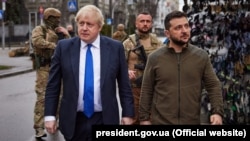 Președintele Ucrainei, Volodimir Zelenski, și premierul Marii Britanii, Boris Johnson, mergând pe străzile aproape pustii ale Kievului, sâmbătă, 9 aprilie 2022. În stânga lui Volodimir Zeleski se vede o plasă de camuflaj.