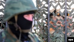 An armed man in military uniform, believed to be Russian, stands outside Ukraine's naval headquarters in Sevastopol. Inside, Ukrainian troops guard the base. 