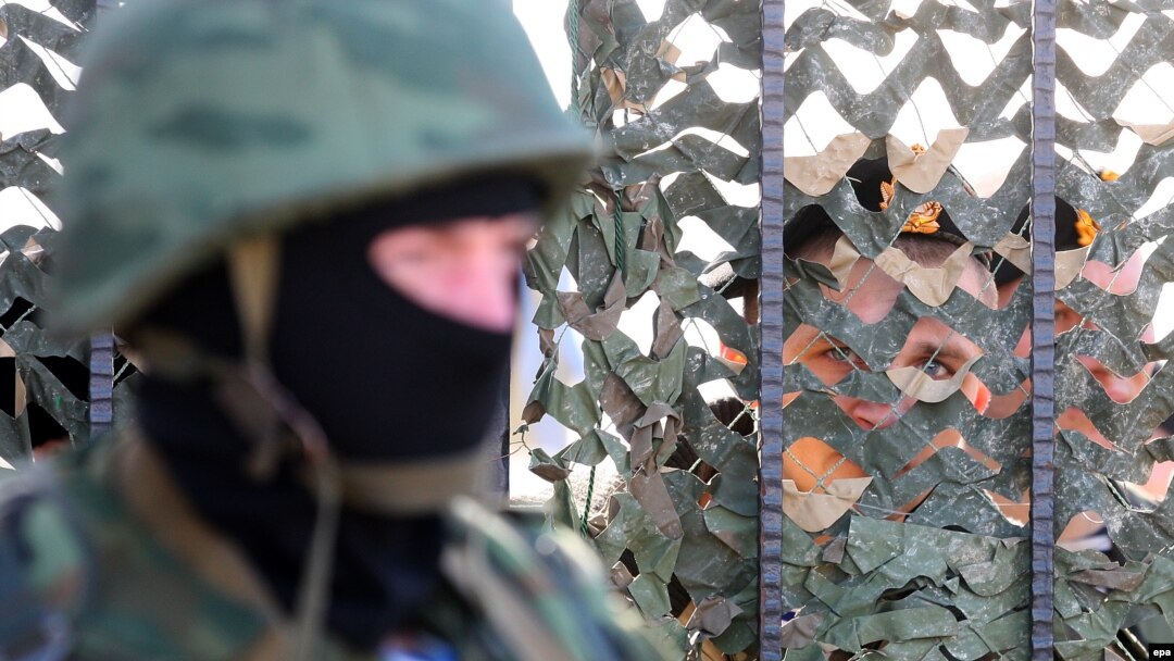 An armed man in military uniform, believed to be Russian, stands outside Ukraine's naval headquarters in Sevastopol. Inside, Ukrainian troops guard the base. 