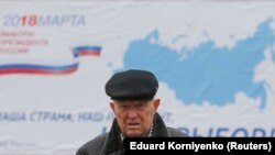 Мужчина на фоне билборда с информацией о дате проведения президентских выборов в России.