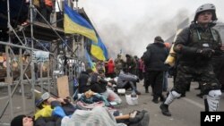 Protestatari se odihnesc in vreme ce alții, in spate, luptă cu poliția pe maidan.