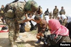 A member of the Kurdish Peshmerga forces helps Yazidis released by IS on the outskirts of Kirkuk on April 8.