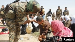 A member of the Kurdish Peshmerga forces helps people from the minority Yazidi sect on the outskirts of Kirkuk on April 8.