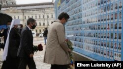 Antony Blinken amerikai külügyminiszter (középen) ukrán kollégájával és a Független Ukrán Egyház metropolitájával közösen virágokat helyez el a Kelet-Ukrajnában elesettek emlékfalánál. Kijev, 2021. május 6-án