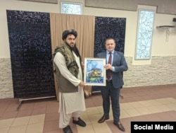 A member of the Taliban delegation receives a painting from an executive from the Belarusian BelAZ company that specializes in heavy machinery.
