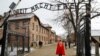 Extremiști de dreapta trecând pe sub poarta pe care scrie "Arbeit Macht Frei" (munca te face liber), poarta lagărului de exterminare de la Auschwitz.