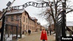 Extremiști de dreapta trecând pe sub poarta pe care scrie "Arbeit Macht Frei" (munca te face liber), poarta lagărului de exterminare de la Auschwitz.