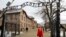 Extremiști de dreapta trecând pe sub poarta pe care scrie "Arbeit Macht Frei" (munca te face liber), poarta lagărului de exterminare de la Auschwitz.