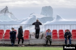 Un ochi la minge, altul la iceberg. Locuitorii se adună la un eveniment sportiv la Qeqertarsuaq, Insula Disko, Groenlanda, pe 30 iunie 2024.