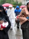 An Afghan woman walks through a market as a Taliban fighter stands guard in Kabul. (file photo)