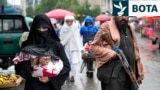 Një grua afgane duke ecur në një treg të vjetër të Kabulit, teksa afër i qëndron një luftëtar taliban.