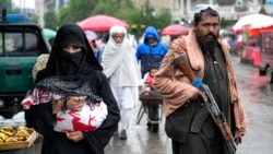 Kabul - o femeie afgană merge la piață în ținuta obligatorie - i se văd doar ochii și mâinile, în timp ce un luptător taliban stă de pază în Kabul (arhivă). 