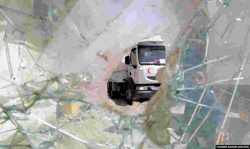 A Red Crescent truck, part of a humanitarian aid convoy, is seen through a hole in glass as it drives toward eastern Ghouta in Syria on March 5. (epa-EFE/Youssef Badawi)