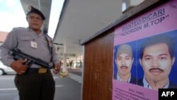 An Indonesian policeman next to a poster of Malaysian fugitive Noordin Mohammed Top, who is allegedly behind a series of suicide bombings in Indonesia dating back to 2003 and is one of Asia's most-wanted and elusive militant leaders.