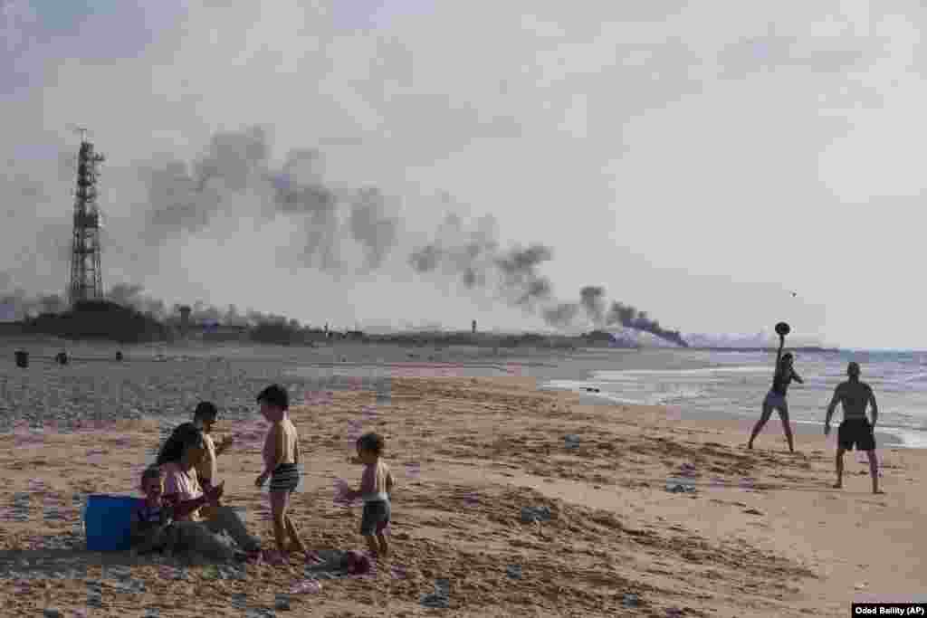 Ізраільцяне на пляжы на мяжы Ізраіля і Газы, на фоне чорнага дыму з шын, падпаленых палестынскімі дэманстрантамі. 