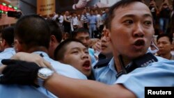 پلیس یکی از معترضان را پس از ضرب و شتم از سوی گروهی از هواداران لباس شخصی چین، از محل دور می‌کند