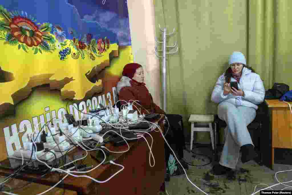 Două femei își încarcă telefoanele într-un „punct al invincibilității”, un adăpost administrat de guvern care oferă servicii de bază și căldură în timpul întreruperilor de curent, pe 10 ianuarie.