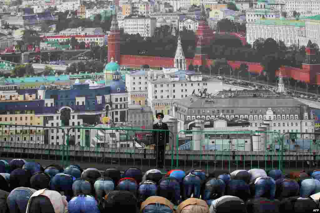 A police officer stands guard in front of a banner depicting Moscow's panorama as Muslims pray on a street in Moscow during the Eid al-Adha festival. (AFP)