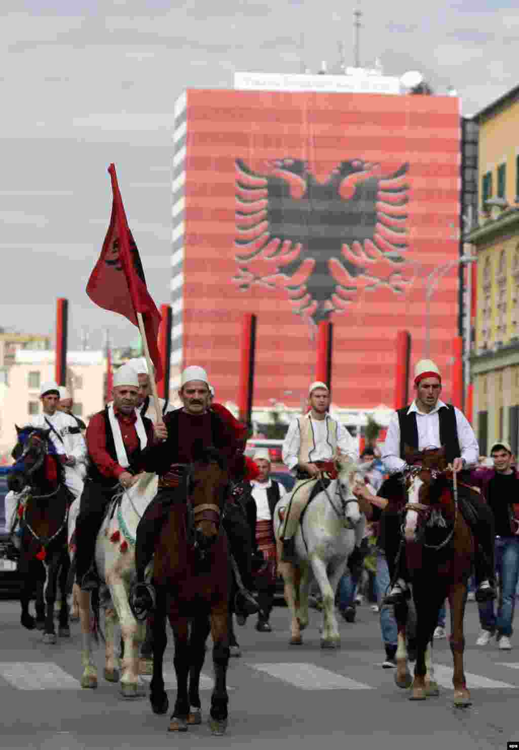 Kosovar Albanian men wear traditional attire as they ride through Tirana.