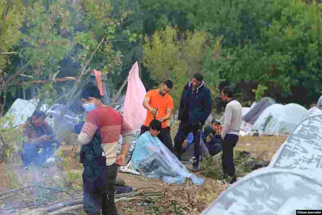 Мигрант-соотечественник стрижет мужчину, также застрявшего в палаточном лагере.
