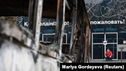 Kazakhstan - A man sits on the steps of a building as a vehicle, which was burnt during mass protests, is seen in the foreground, in Almaty, January 9, 2022.