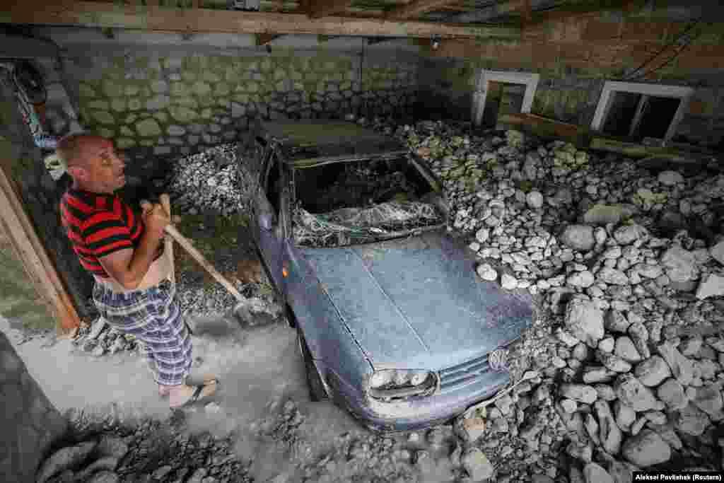 Мужчина стоит рядом с автомобилем, поврежденным наводнением после сильного дождя в Ялте, Крым