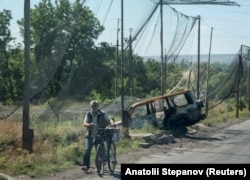 A man wheels his bicycle down a road in Druzhkivka covered with anti-drone netting and surrounded by razor wire on June 21. The wire is in place as a preparatory measure for a potential ground battle for the town.