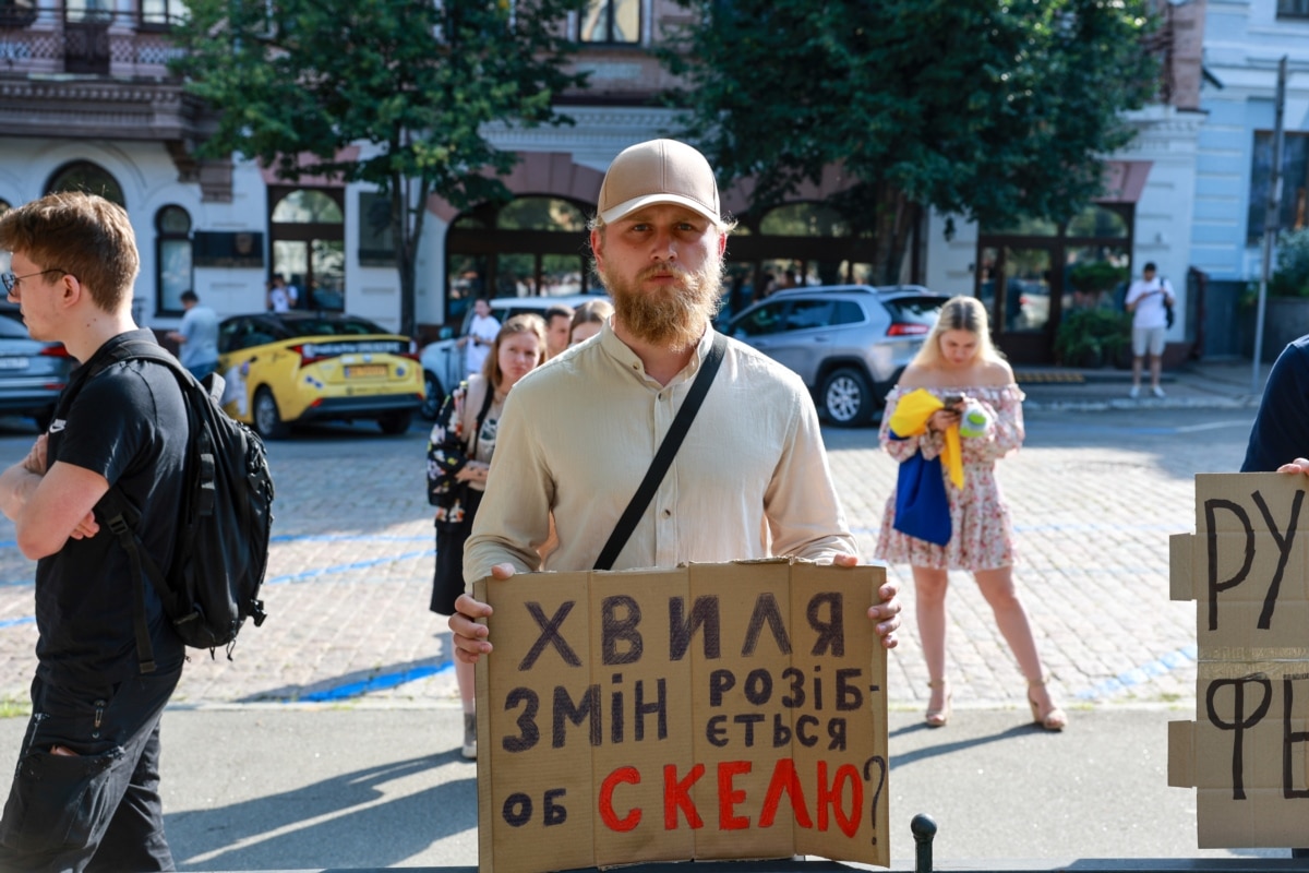 Чоловік тримає банер з написом, де є згадка про полк «Скеля».<br><br>23 червня видання <a href="https://babel.ua/texts/127938-shturmoviy-polk-skelya-maye-boyovi-zaslugi-i-dobre-zabezpechennya-a-shche-kazhut-ochevidci-tam-katuyut-i-zabivayut-lyudey-na-smert-rozsliduvannya-babelya" target="_blank" class="wsw__a">«Бабель» опублікувало матеріал, </a>у якому, серед іншого, йдеться, що за останні пів року в навчальних центрах «Скелі» було 26 смертельних випадків. Більшість із померлих чоловіків не пробула в полку й місяця, а офіційна причина смерті здебільшого – пневмонія. Крім того, журналісти повідомили про систематичні катування і побиття в полку. Зараз триває розслідування щодо достовірності цих тверджень