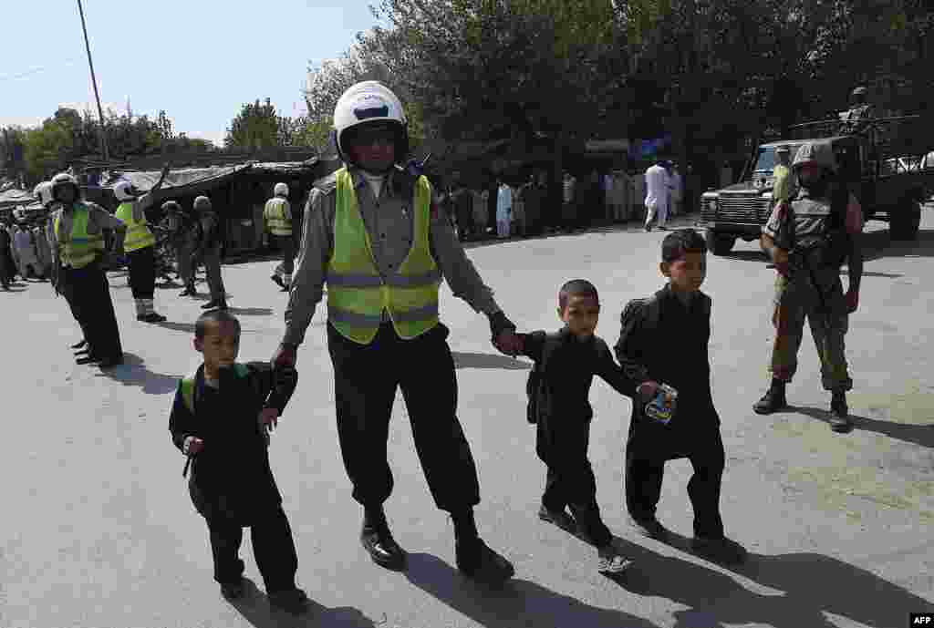 A traffic policeman helps schoolchildren cross the road on September 2 as soldiers stand guard after suicide bombers attacked a Christian neighborhood in Khyber Agency near Peshawar, Pakistan. (AFP/A. Majeed)