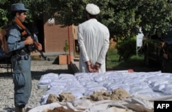 Полицей тұтқындалған есірткі сататын адамды күзетіп тұр. Ауғанстан, 19 қыркүйек 2013 жыл.