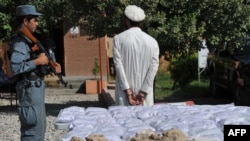 Afghanistan - An Afghan policeman (L) stands guard as a detained suspect and bags containing heroin are presented to the media at a police station in Jalalabad on September 19, 2013