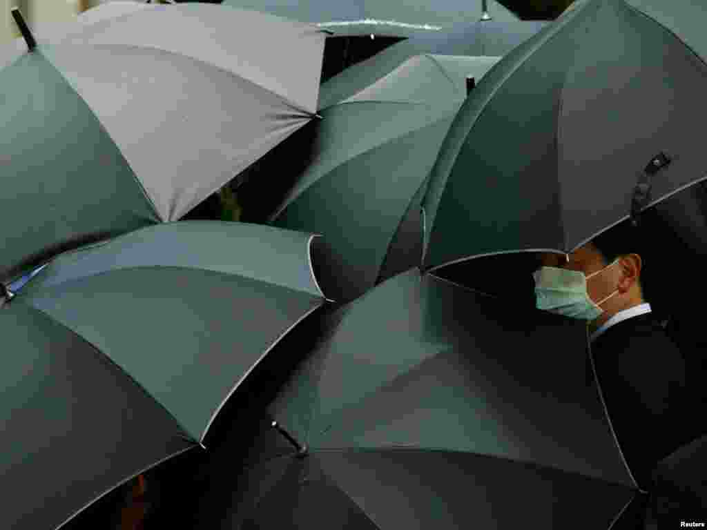 A mourner wearing a mask to ward off SARS hides under an umbrella during the funeral of SARS doctor Tse Yuen-man in Hong Kong May 22, 2003. Tse, the first front-line doctor to be killed by the disease in the territory, was given the highest honors at her funeral and was buried in Gallant Garden, a cemetry reserved for residents who perish in the line of duty. The deadly virus has infected 1,719 people and killed 255 since it swept into the congested territory. REUTERS/Bobby Yip 